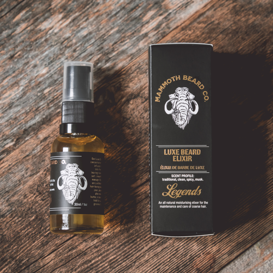 A bottle of Luxe Beard Elixir by Mammoth Beard Co. placed next to its packaging box on a wooden surface.