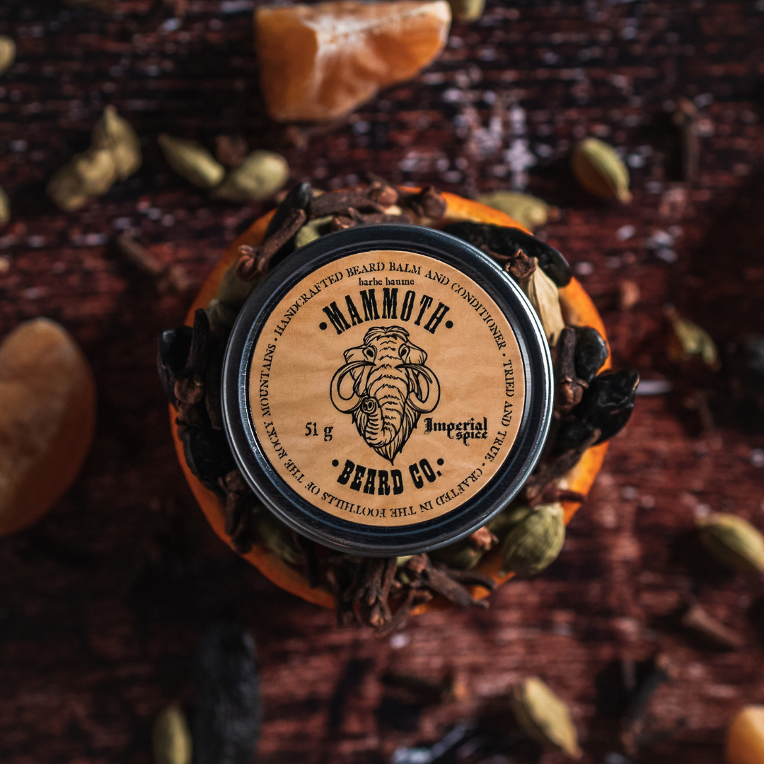 Mammoth Beard Co. Imperial Spice Beard Balm tin surrounded by clove, cardamom, and citrus on a rustic wooden surface, highlighting its warm autumn-inspired scent.