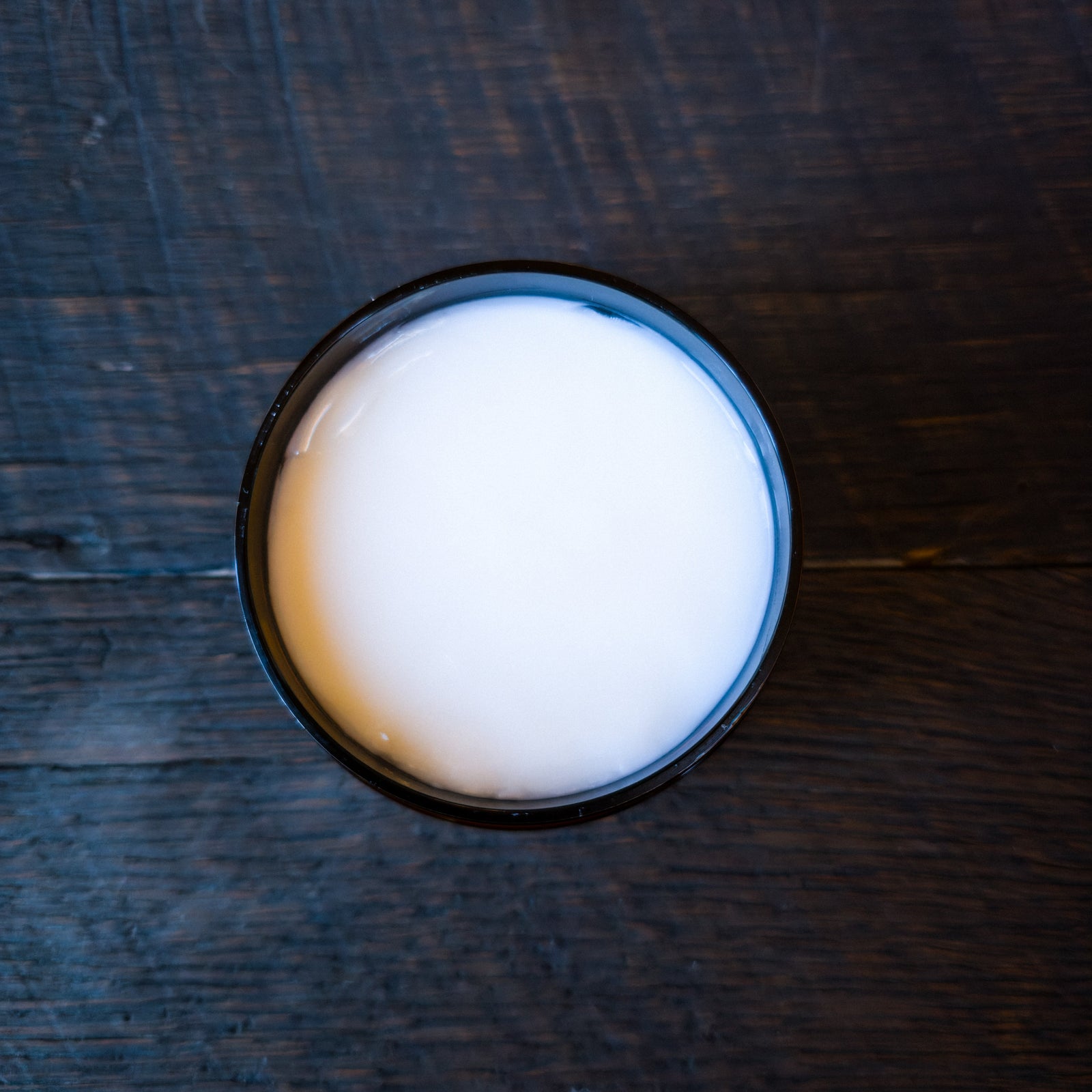 A top-down view showing Super Soft Beard Conditioner in an amber jar, placed on a dark wooden surface.