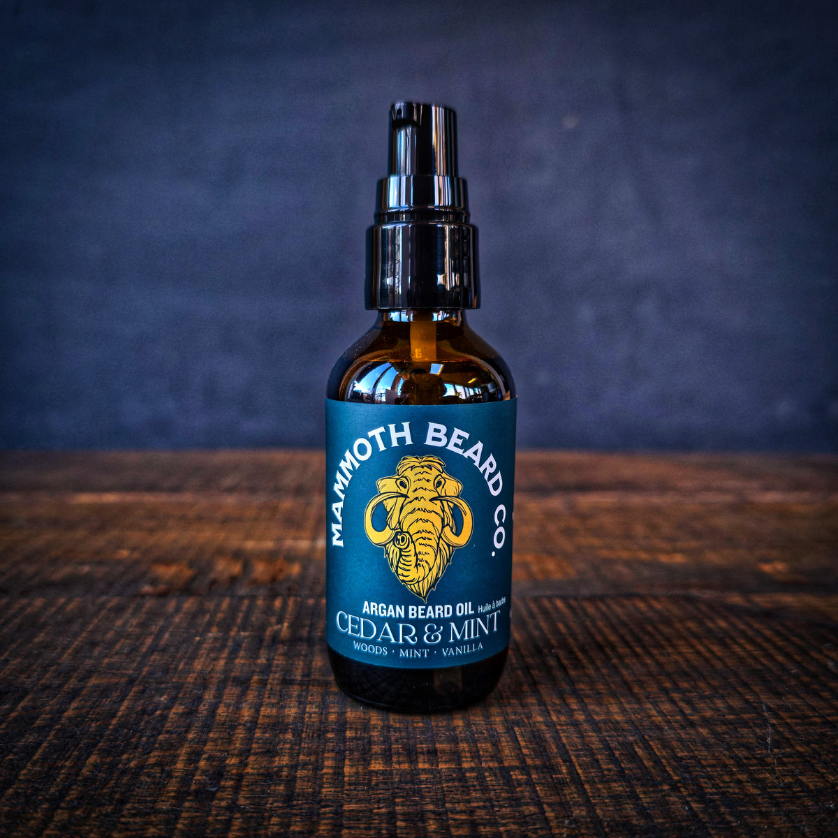 Close-up of Mammoth Beard Co Cedar &amp; Mint Argan Beard Oil pump bottle on dark wooden surface, premium natural beard oil for hydration and shine.