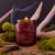 Highland Ember candle by Mammoth Beard Co. burning with a crackling wood wick, surrounded by moss and antlers, evoking a rustic smoky whiskey and moss-covered earth scent.
