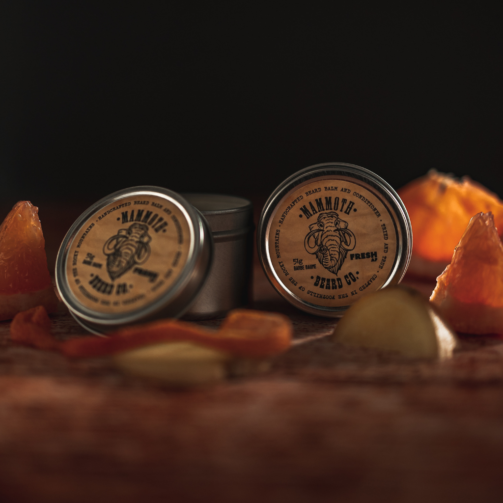 Mammoth Beard Co. Fresh AF Beard Balm tins styled with orange slices, citrus peel, and ginger on a rustic wooden surface, showcasing its bright and invigorating scent.