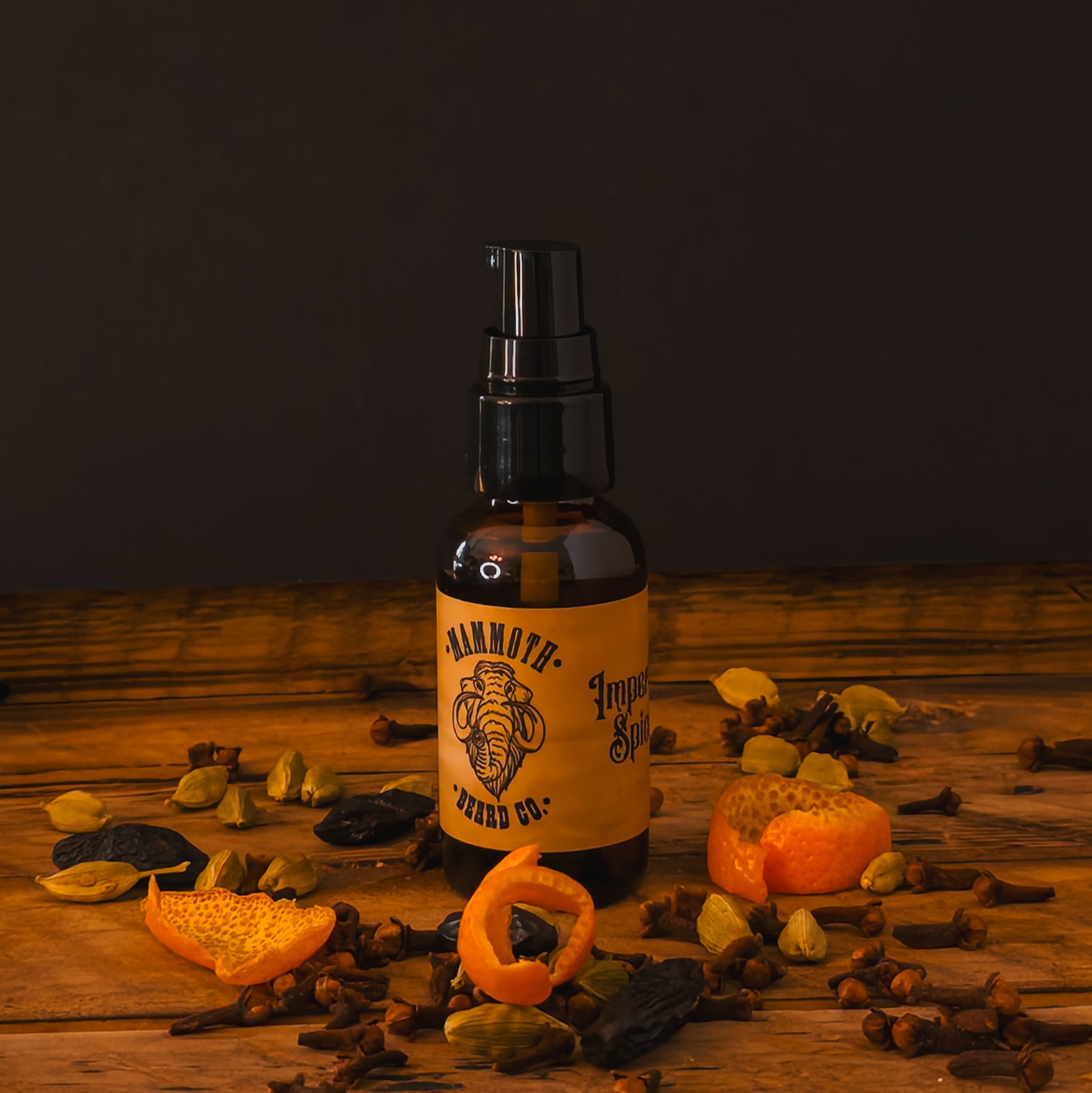 Mammoth Beard Co. Imperial Spice Beard Oil bottle surrounded by dried orange peel, clove, and cardamom on a rustic wooden surface, showcasing its warm, spiced autumn aroma.