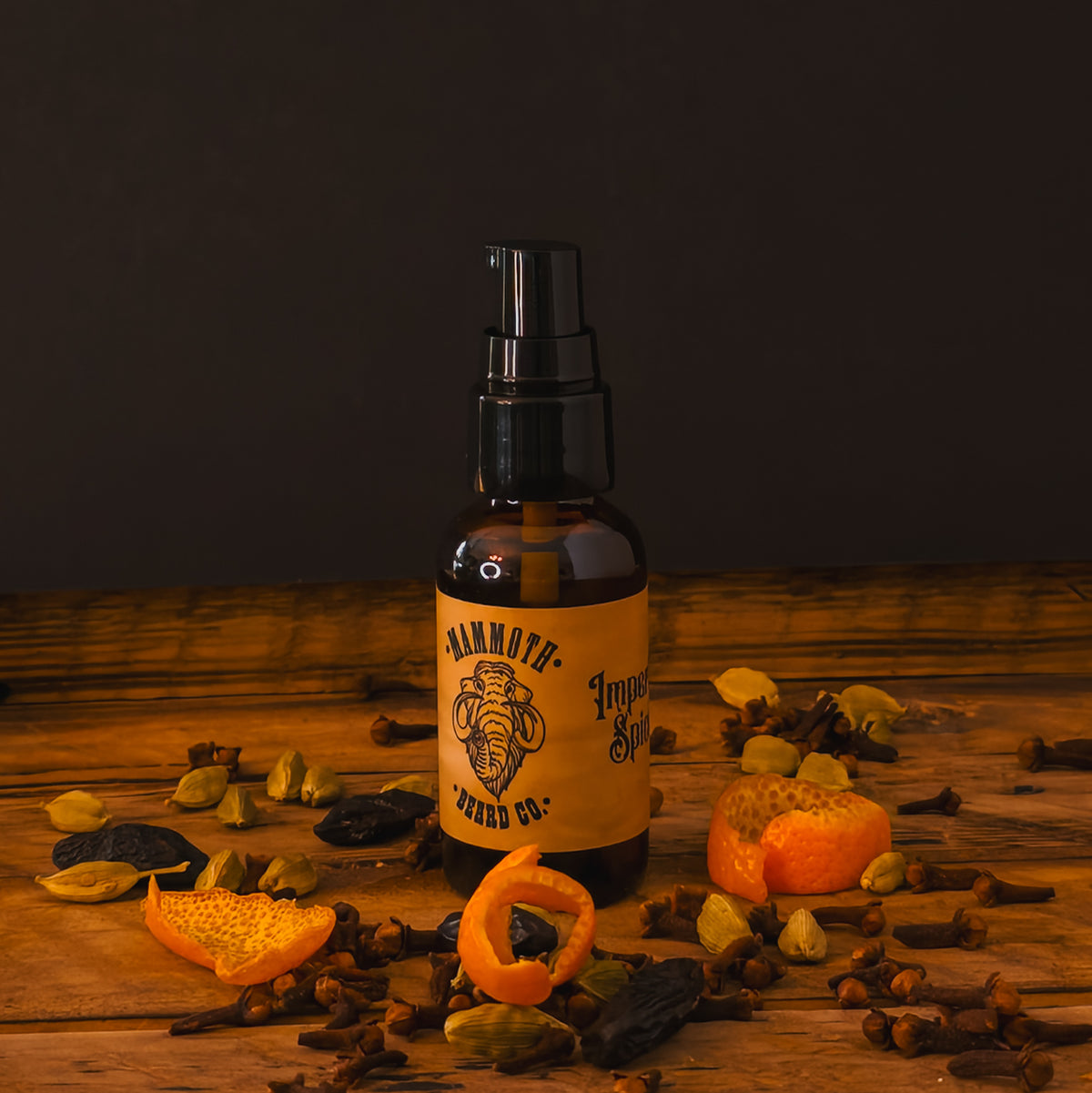 Mammoth Beard Co. Imperial Spice Beard Oil bottle surrounded by dried orange peel, clove, and cardamom on a rustic wooden surface, showcasing its warm, spiced autumn aroma.
