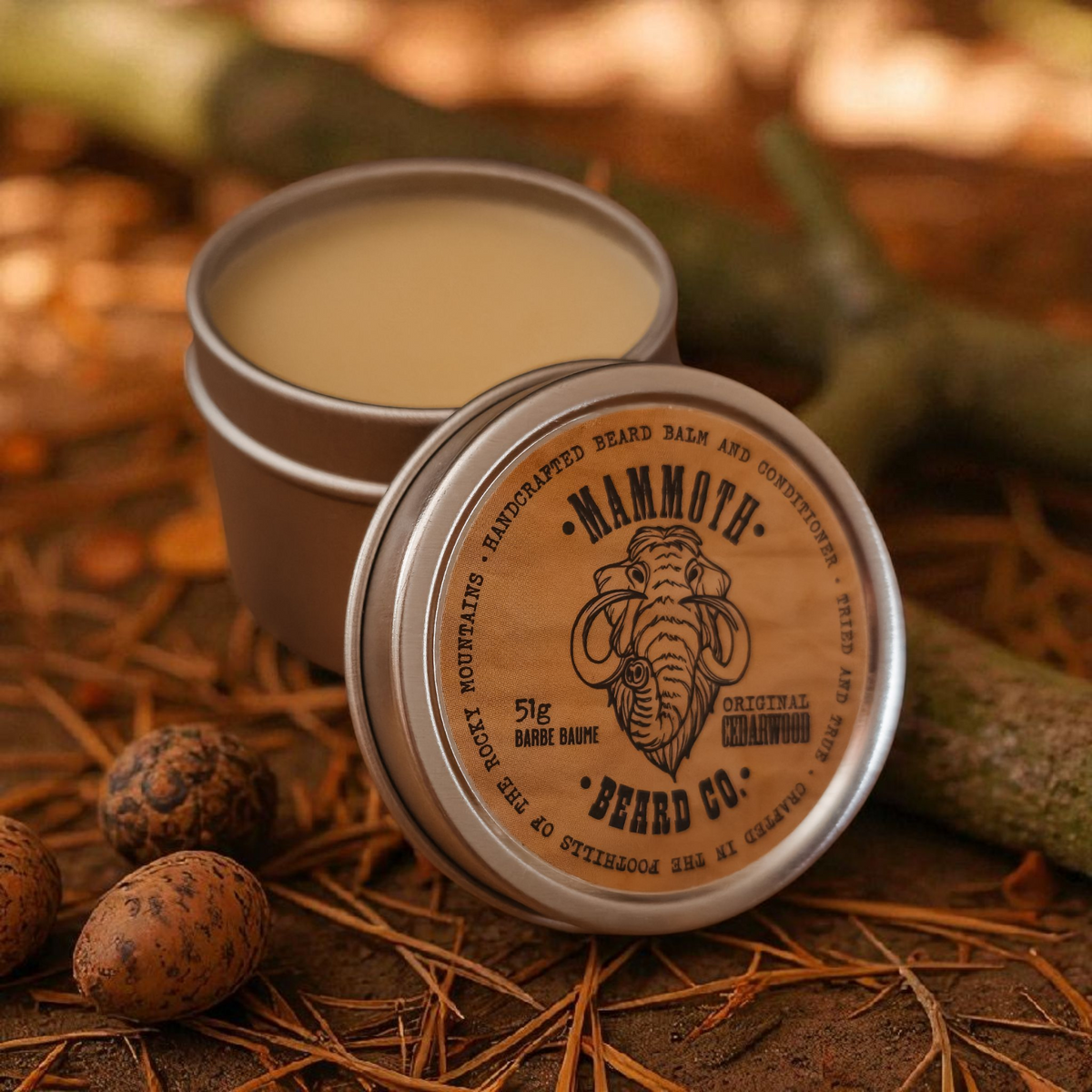 Mammoth Beard Co. Original Cedarwood Beard Balm in a metal tin with rustic outdoor forest background, handcrafted conditioning balm for softening and styling beards.