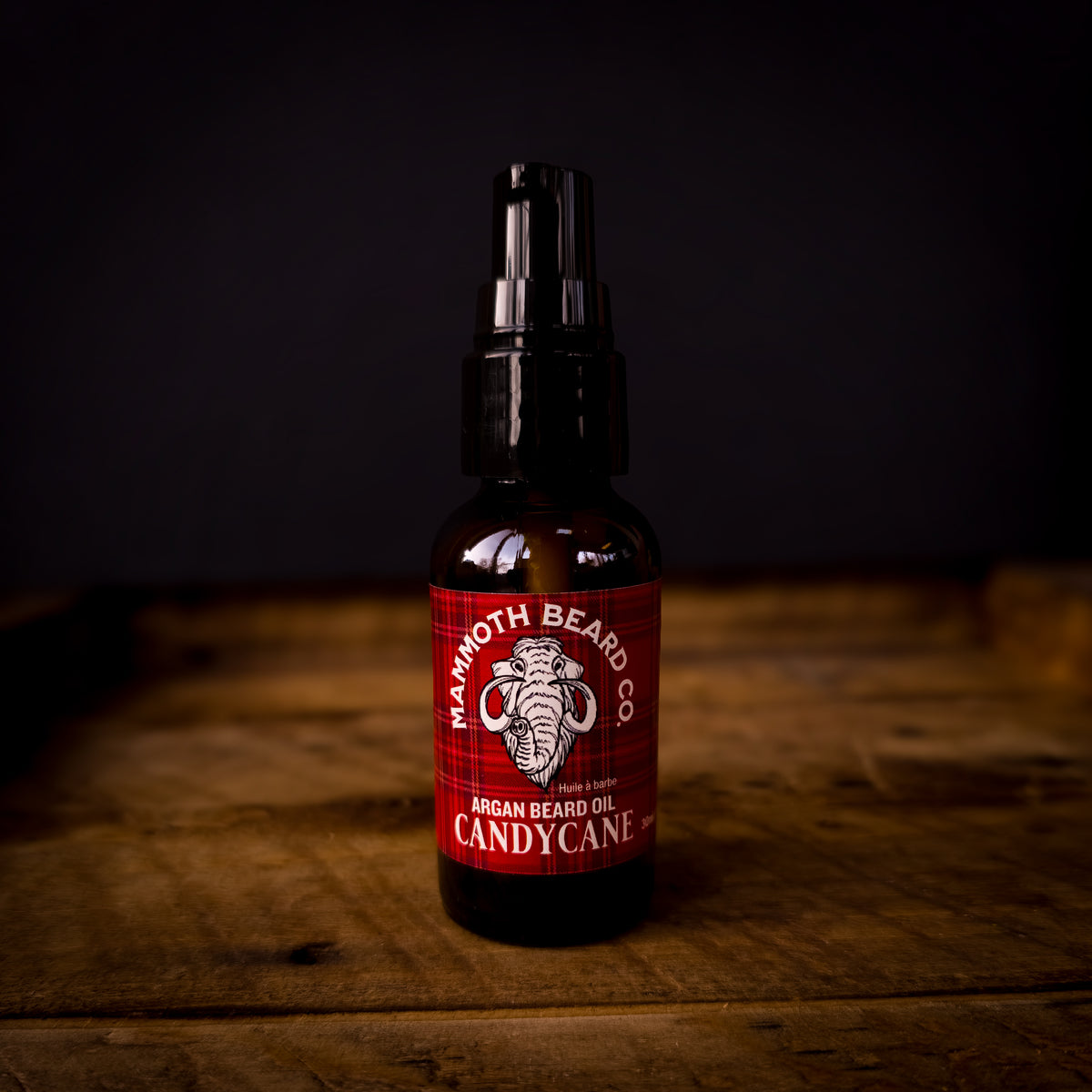 Mammoth Beard Co Candy Cane Argan Beard Oil bottle with red plaid label on rustic wood surface, festive peppermint scent.