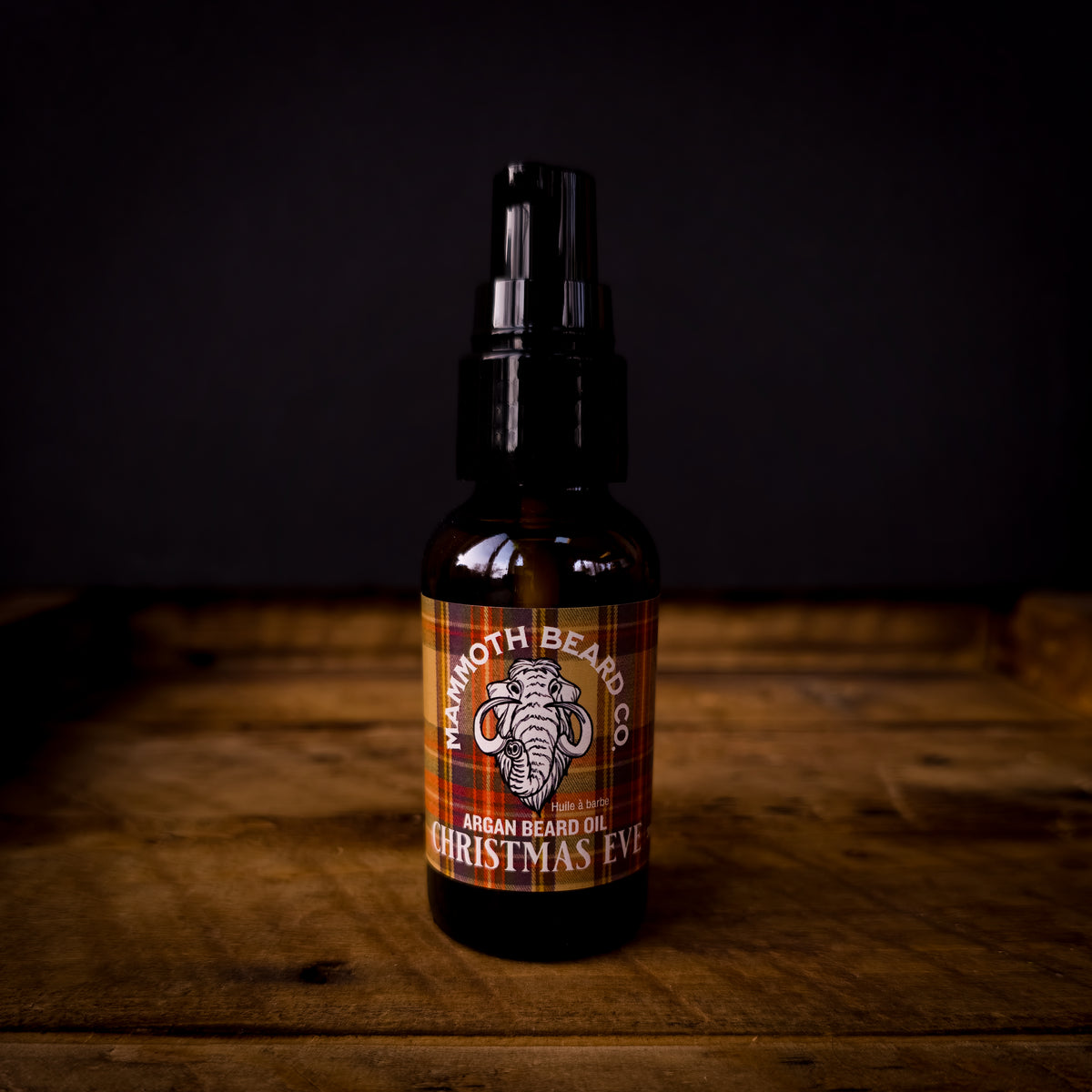 Mammoth Beard Co Christmas Eve Argan Beard Oil bottle with red and gold plaid label on wooden surface, warm spiced festive scent
