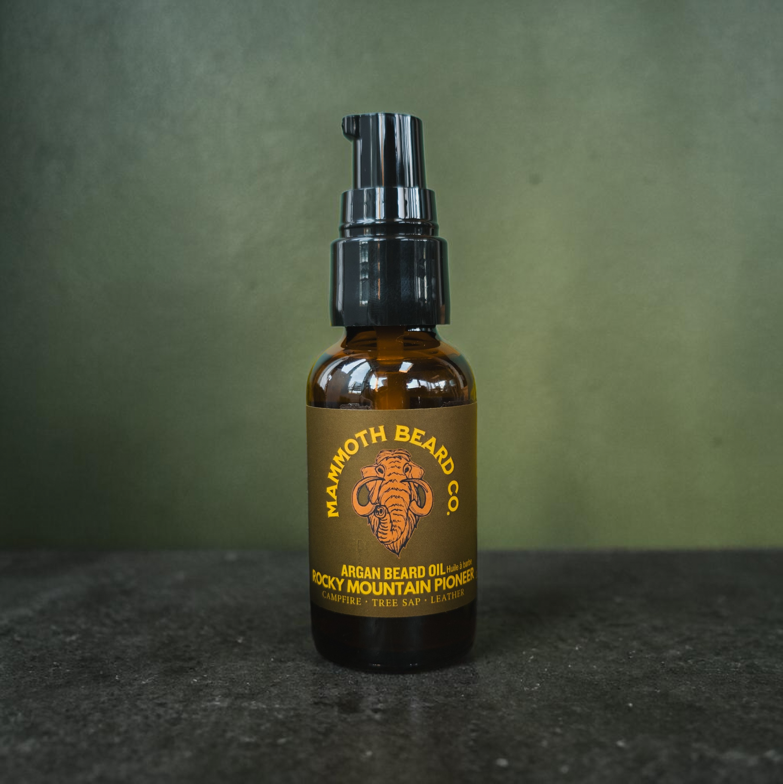 Bottle of Mammoth Beard Co. argan beard oil on a dark surface with a green background