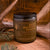 4 oz Rocky Mountain Pioneer natural soy wax candle with lid on, set against rustic wood and antlers, surrounded by evergreen sprigs.
