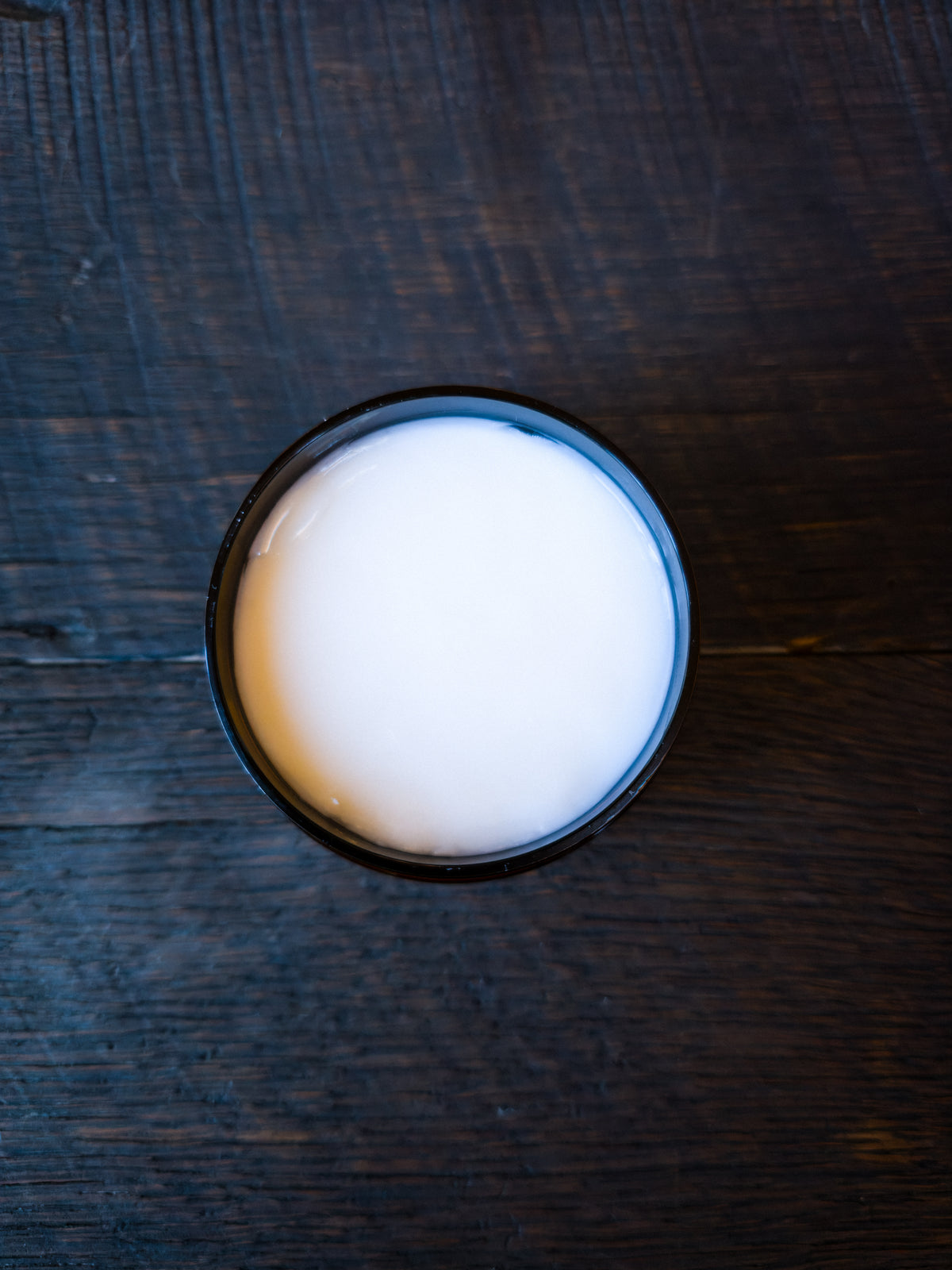 A top-down view showing Super Soft  Beard Conditioner in an amber jar, placed on a dark wooden surface.