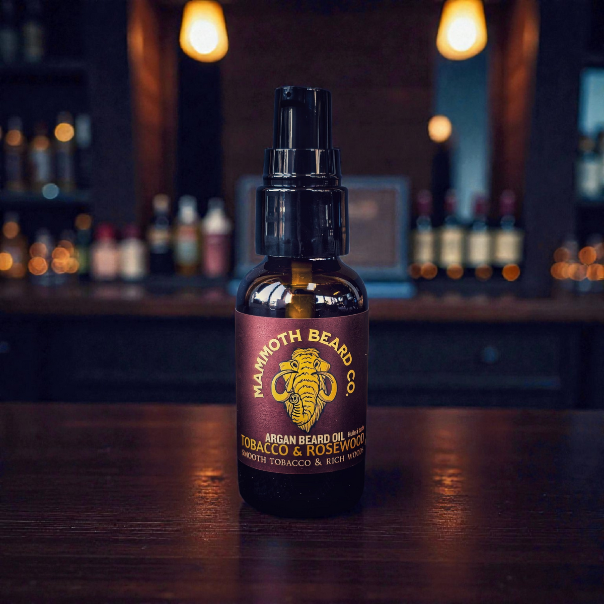 Mammoth Beard Co. Tobacco &amp; Rosewood Argan Beard Oil in 30ml amber glass pump bottle on wood bar top, featuring smooth tobacco and rich rosewood essential oil blend for conditioning and softening beards.