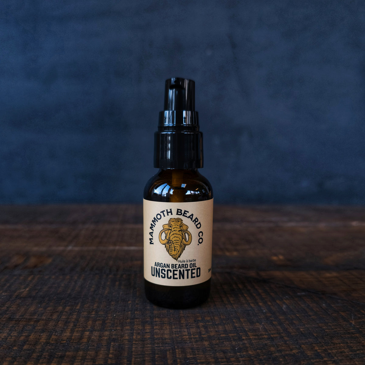 Bottle of Mammoth Beard Co. unscented argan beard oil on a dark textured surface with a dark background.