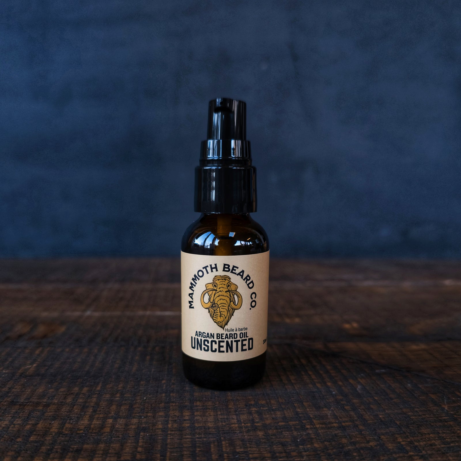 Bottle of Mammoth Beard Co. unscented argan beard oil on a dark textured surface with a dark background.