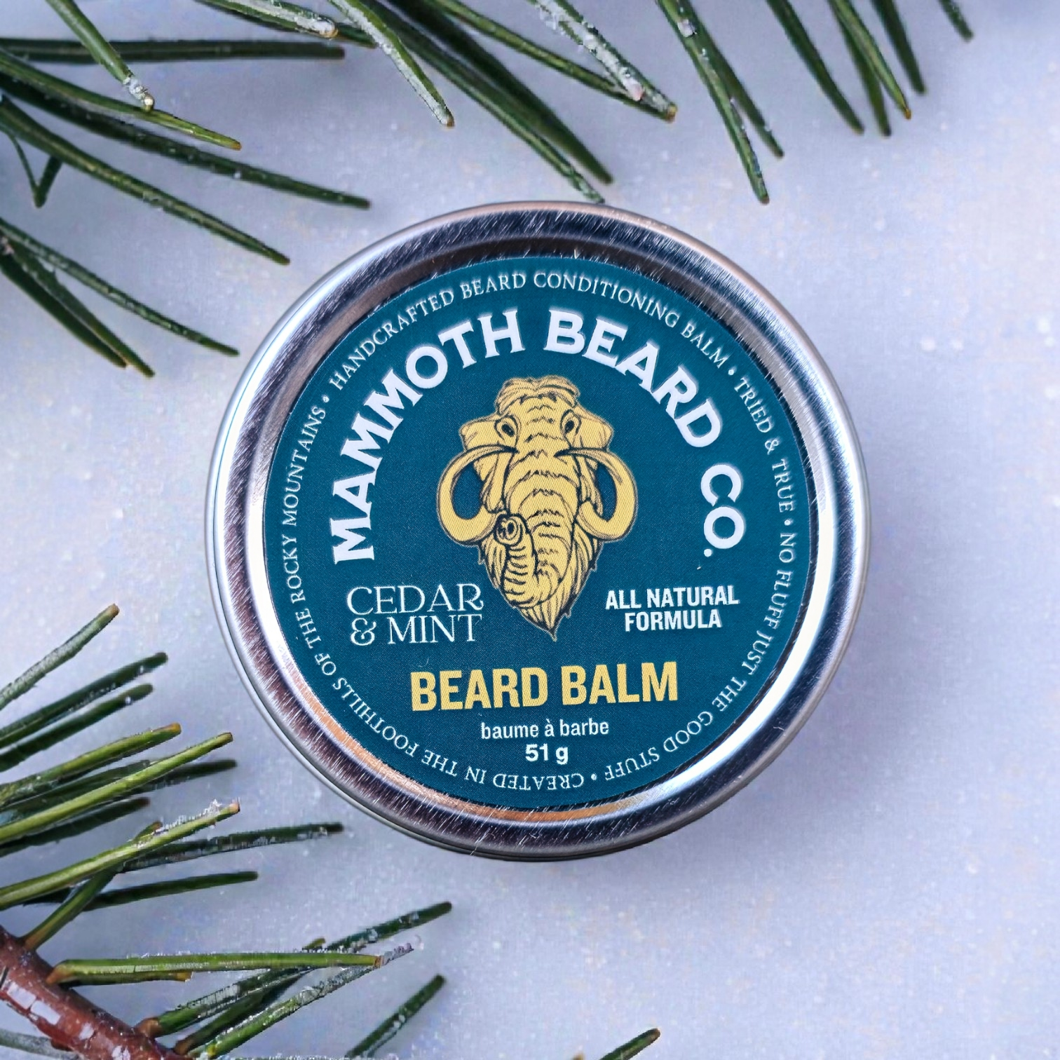 Mammoth Beard Co. beard balm tin with cedar and mint scent on a light background with greenery.